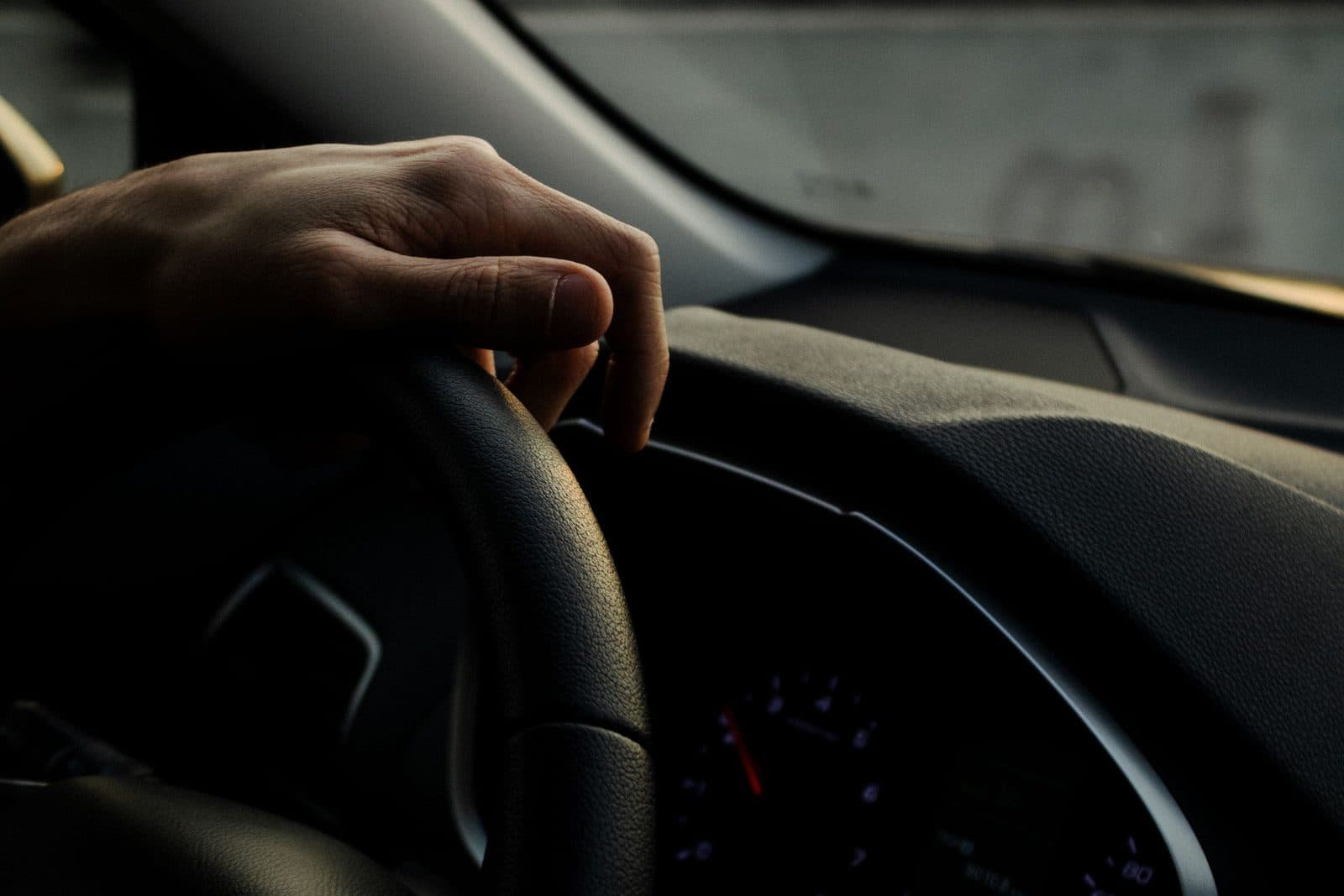 Close-up of a hand on a car's steering wheel with the dashboard in view